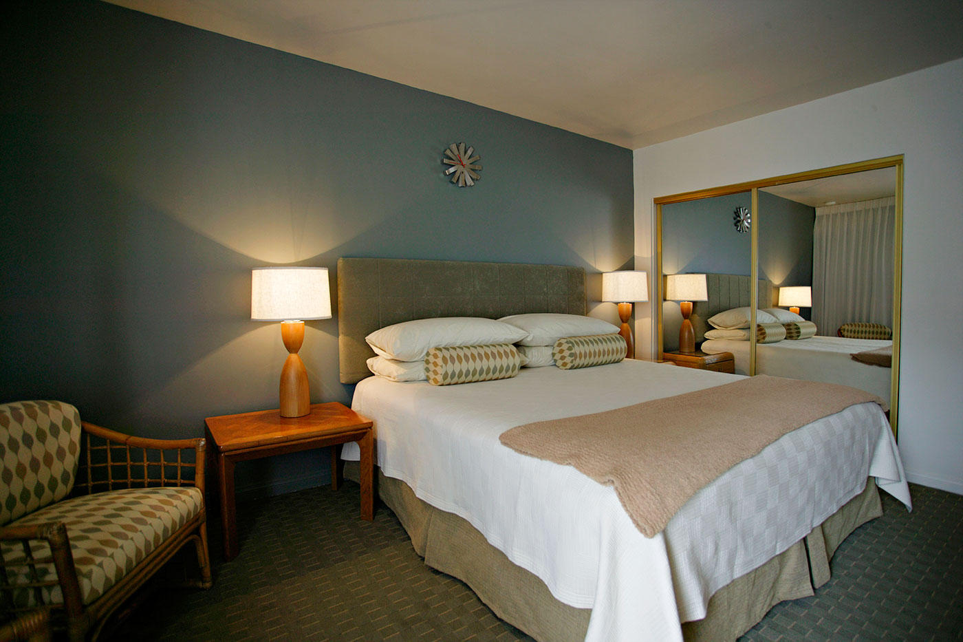 A hotel room with a bed, nightstand, lamp, mirror, and chair.