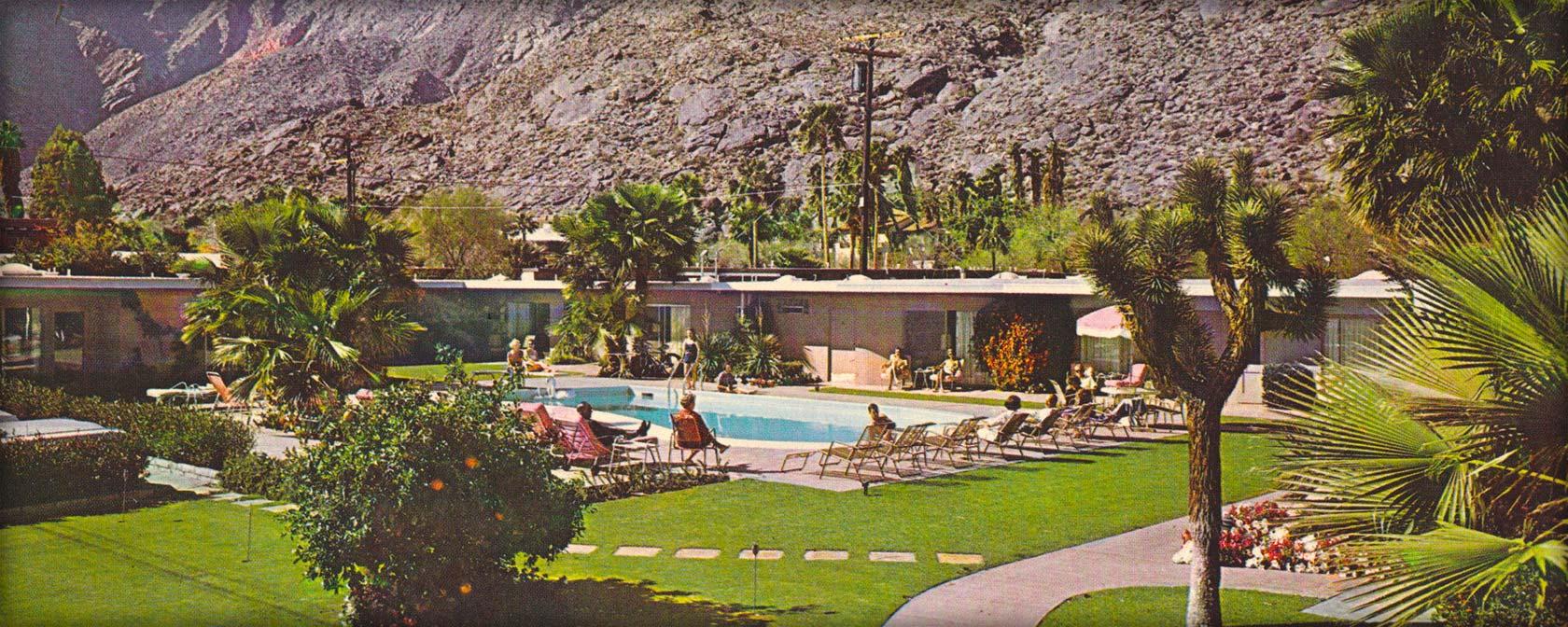A vintage photo of a hotel exterior with a pool, lounge chairs, and palm trees in front of a mountain view.